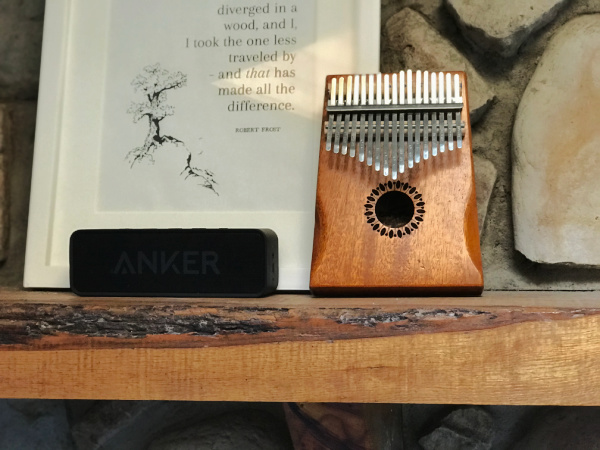kalimba, white picture frame with quote, and anker speaker on mantle