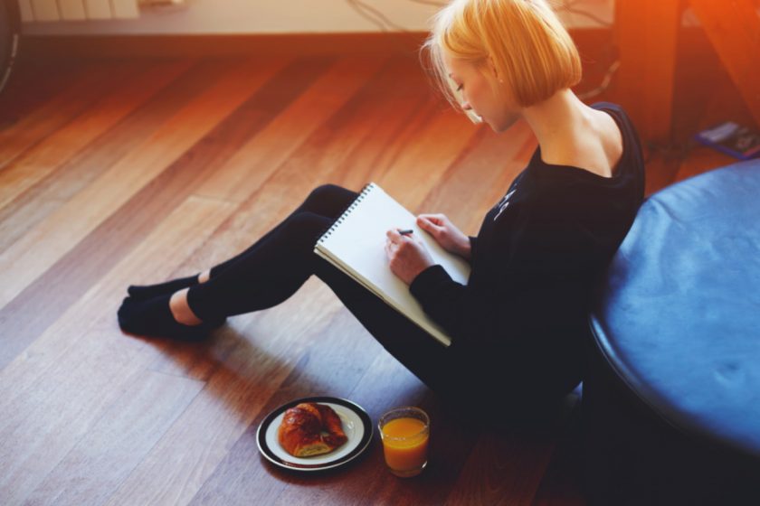 depressed stay at home mom sitting on floor, writing in journal, with orange juice and croisant