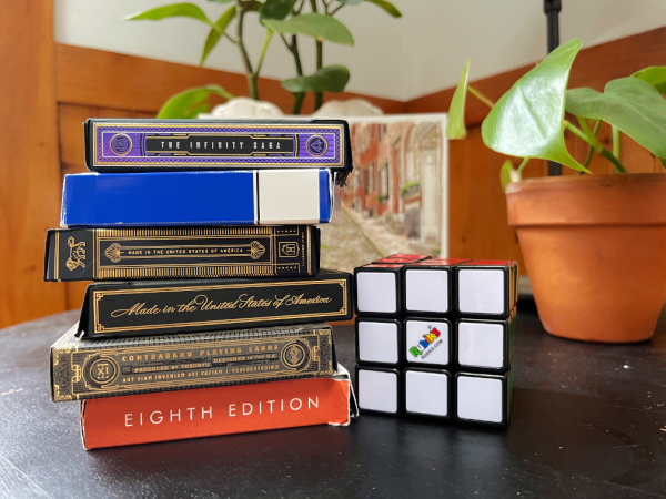 stack of playing cards and rubix cube on black table with plants in background