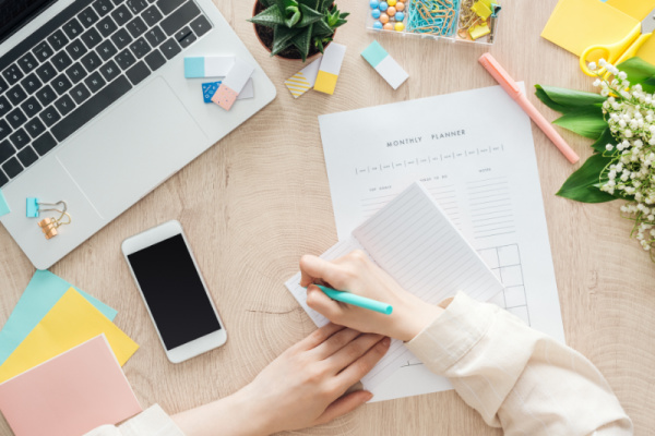 homeschool mom writing in notebook with monthly calendar on desk