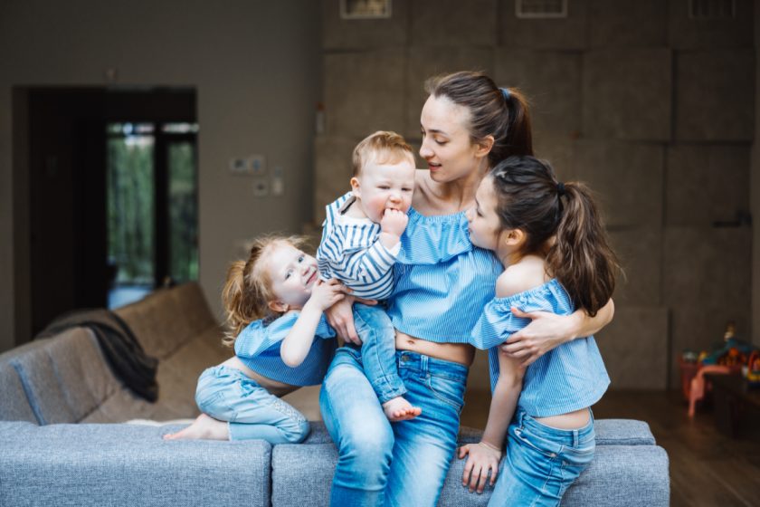 homeschool mom with three kids, including baby and toddler clinging to her while sitting on back of couch