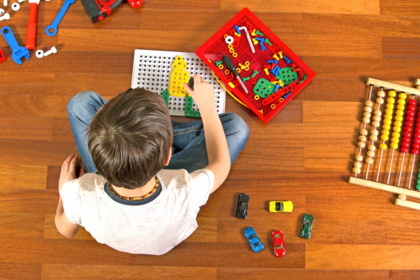 older boy playing with a drill toy set, matchbox cars and abacus on wooden floor
