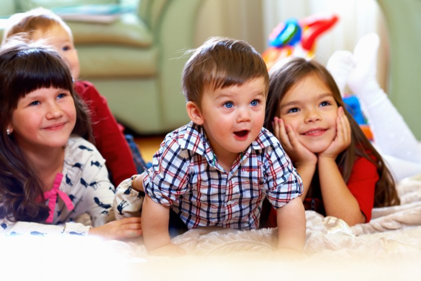 four kids, elementary aged down to toddler, on floor looking up at tv screen