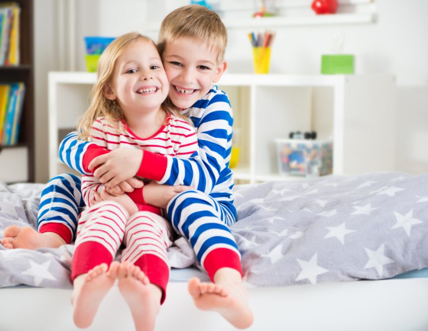 brother and sister dressed up in striped pajamas hugging and sitting on bed together