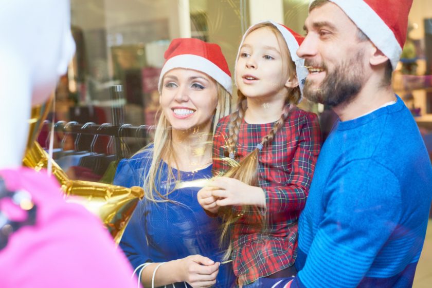 mom and dad holding child, all wearing Santa hats, out Christmas shopping together