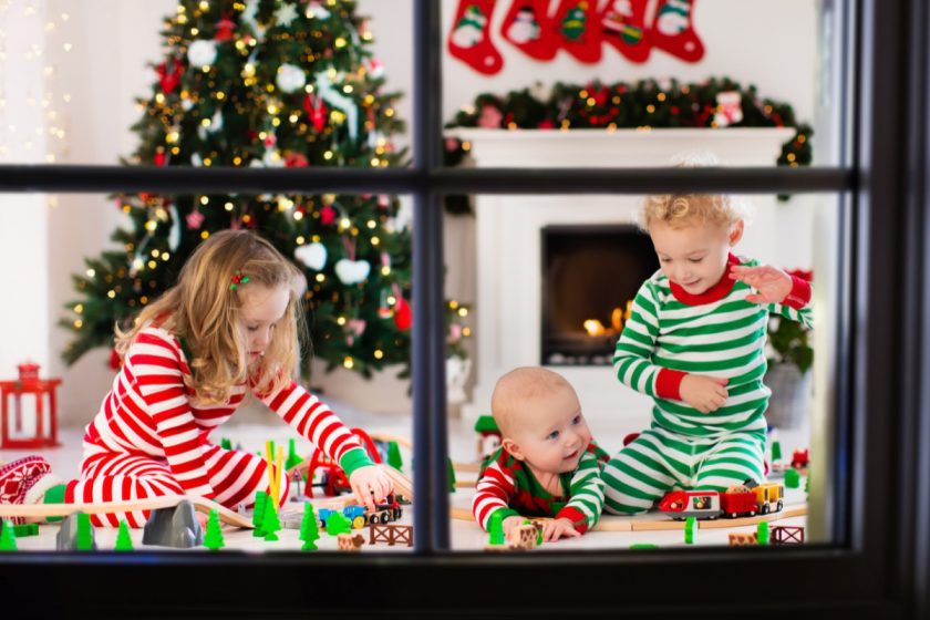 Happy young siblings in matching pajamas playing with Christmas presents - wooden toy railroad and car. 