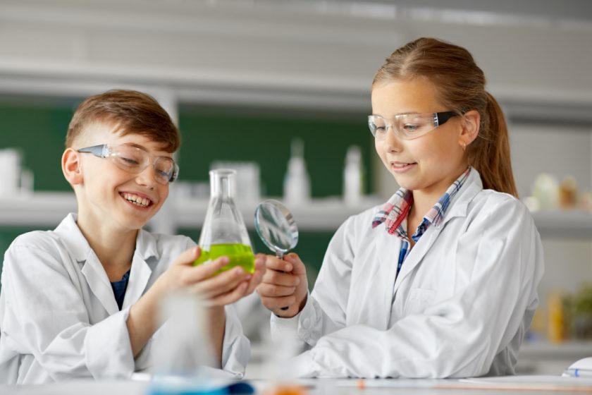 10 year old boy and girl doing a science experiment with a magnifying glass and beakers