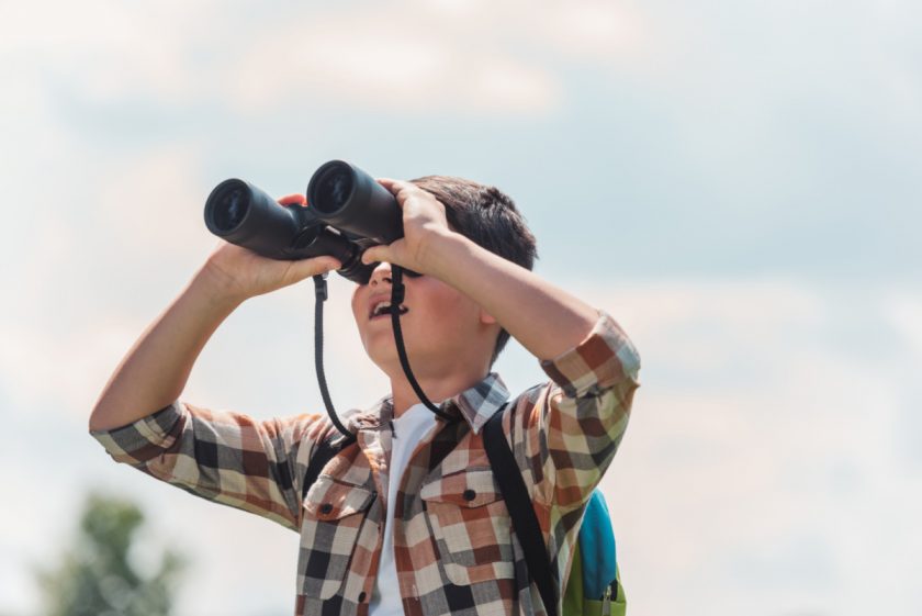 10-year-old boy outside holding binoculars up to eyes