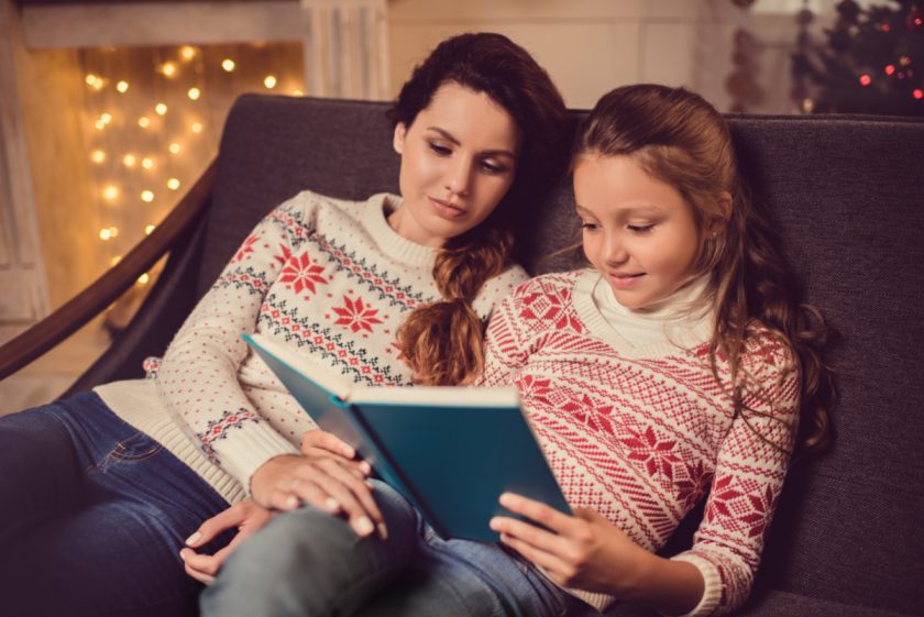 mom and daughter sitting on couch reading on christmas eve