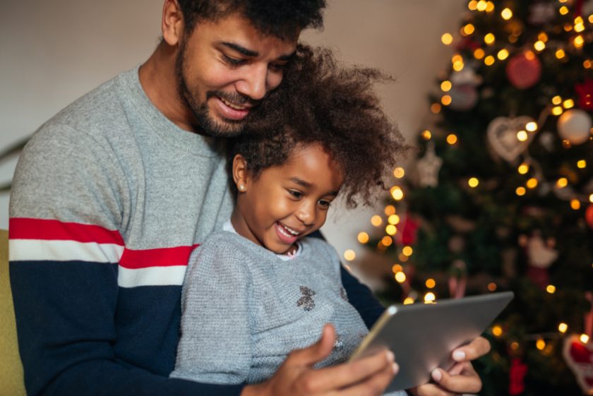 dad and daughter watching a christmas movie on a tablet next to christmas tree