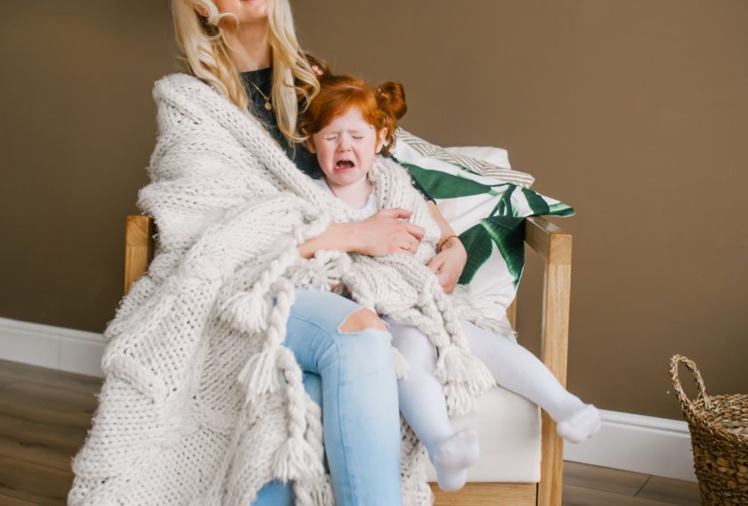 red-headed little girl crying while mom holds her