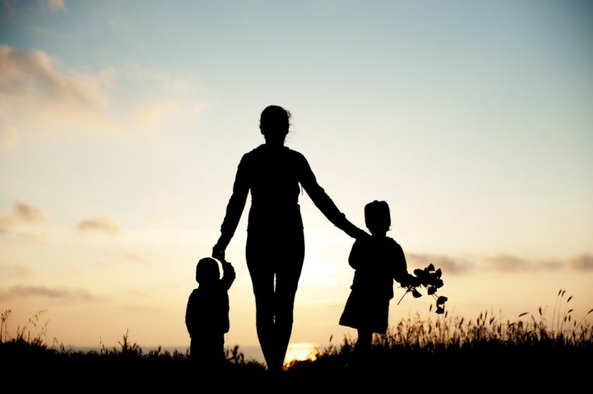 silhouette of mom holding hands with two children at dusk