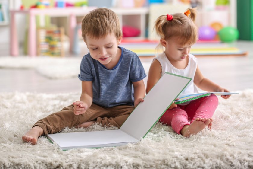 Cute funny children reading books while sitting on carpet at home