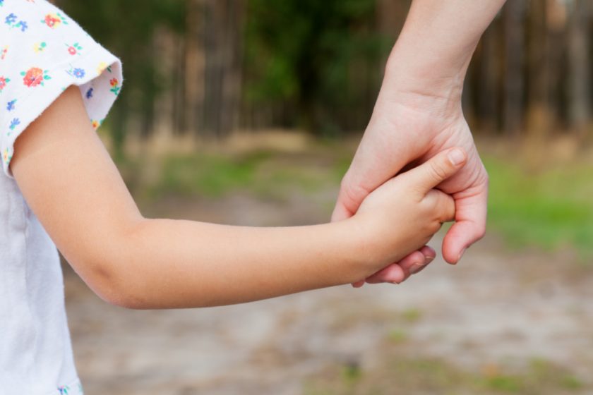 mom and child holding hands outside, selective focus on hands
