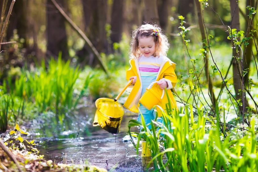 little girl in yellow raincoat walking in stream with bucket and net