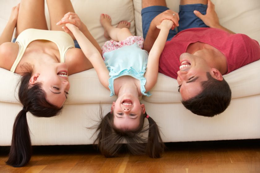 smiling parents and daughter lying on a couch with heads upside down