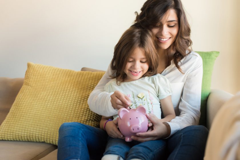 Mother and daughter putting coins into piggy bank, saving money on unschooling concept