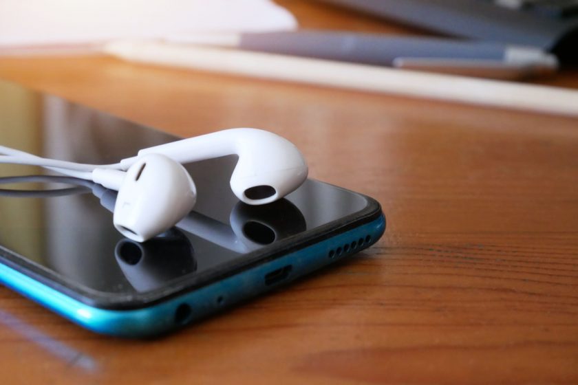 close-up of smartphone with earbuds on table for listening to unschool podcasts