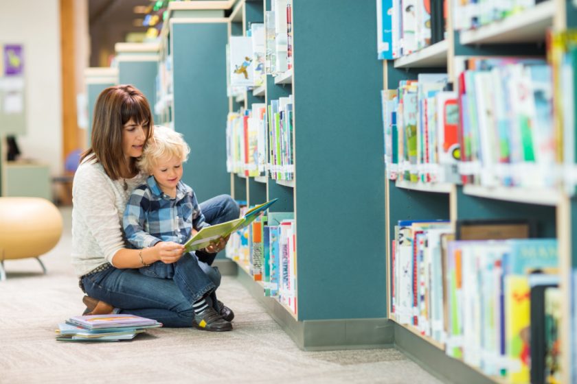 mom holding young child at the library, reading picture book