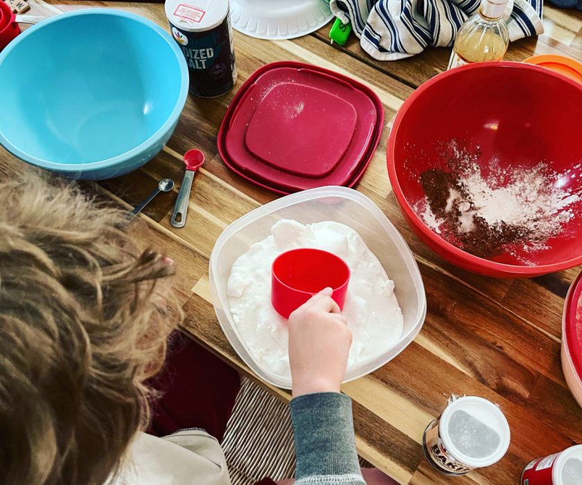 unschooled child doing baking experiment, measuring various ingredients into bowl on table