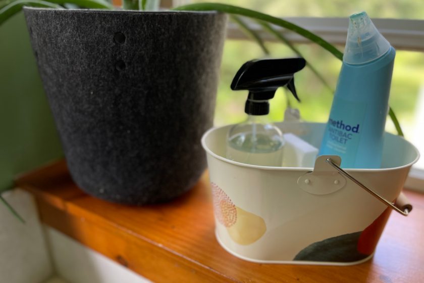 cleaning caddy with bathroom cleaning supplies, sitting on bathroom windowsill next to aloe plant