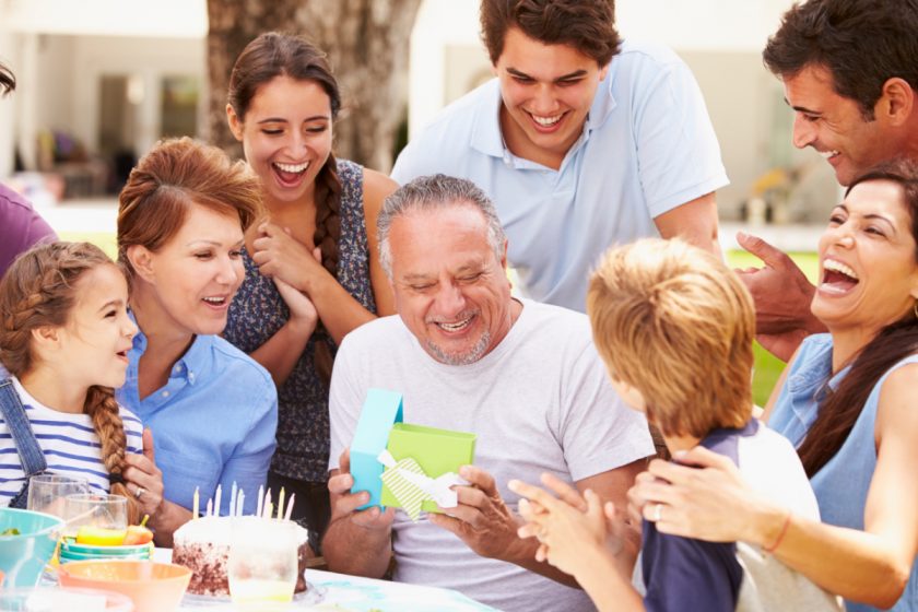 grandfather surrounded by family and grandchildren opening a birthday gift