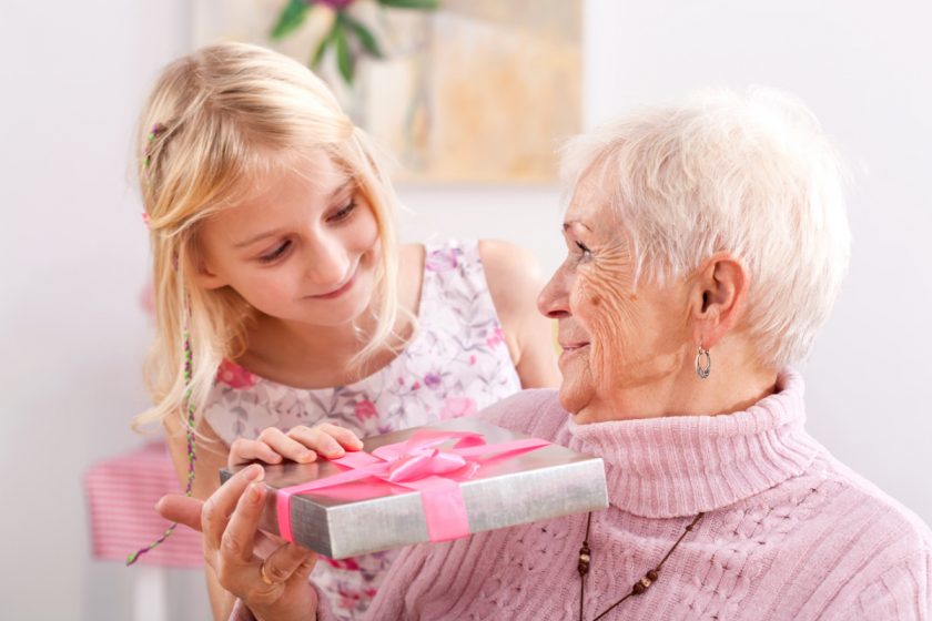 granddaughter giving smiling grandmother a birthday gift (even though she has everything)