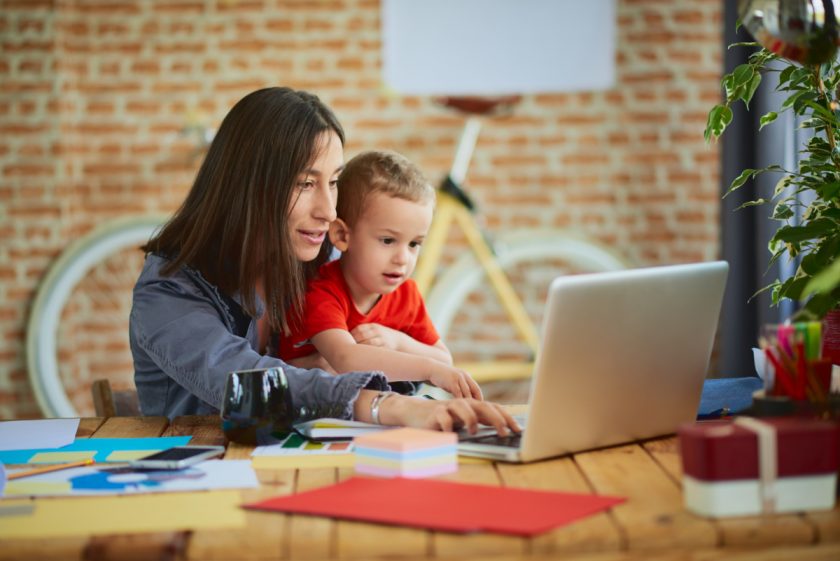 work at home mom holding small child on her lap while working on her laptop