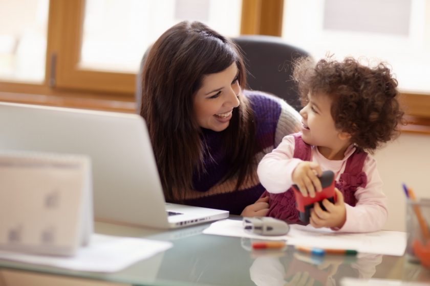 Mom and businesswoman working with laptop computer at home and playing with her baby girl. Horizontal shape, front view, waist up