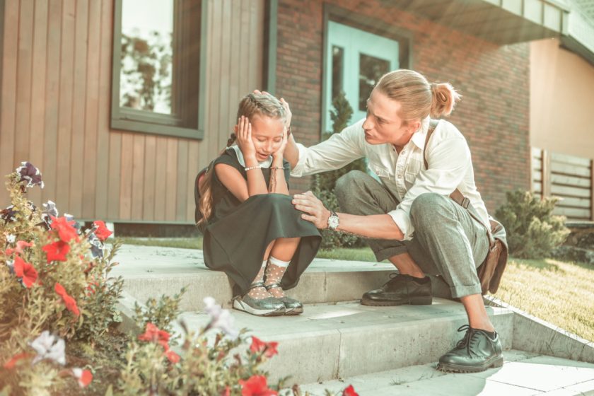 little girl sitting on front steps crying with dad trying to comfort her