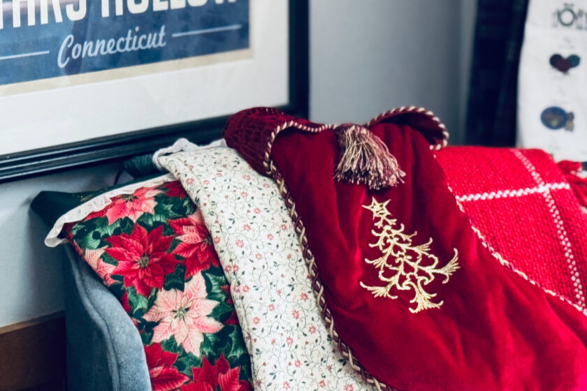 red, white and green stockings on back on chair with red blanket in background.