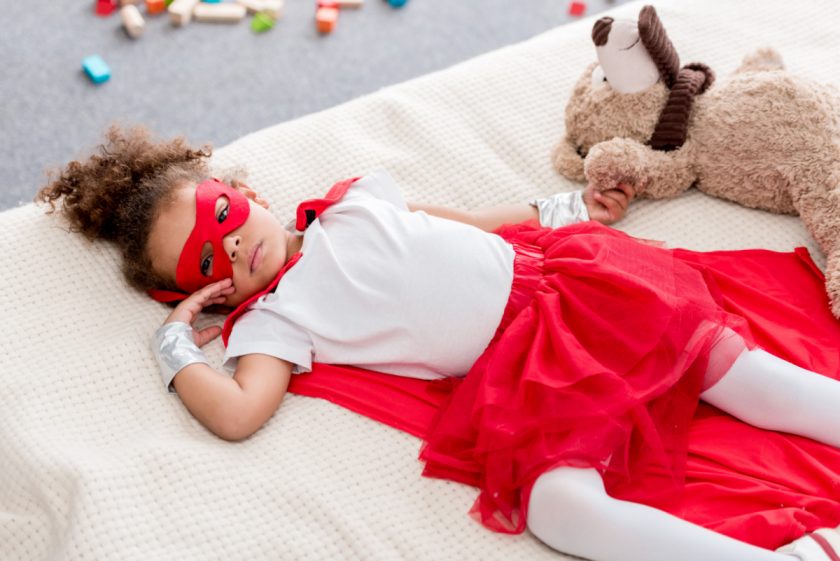 preschool aged girl in super hero costume taking a break and resting on her bed