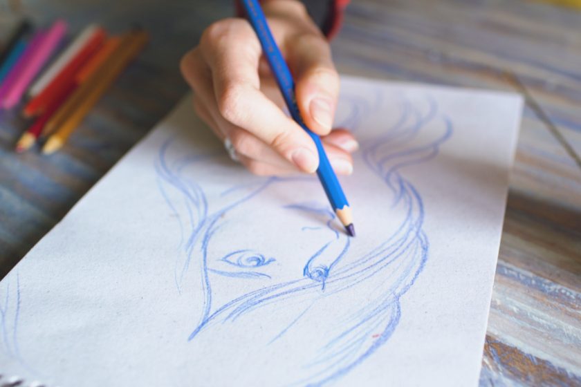 artist drawing woman's face with blue colored pencils