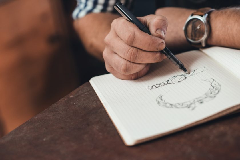 man sketching with pen in graph paper notebook