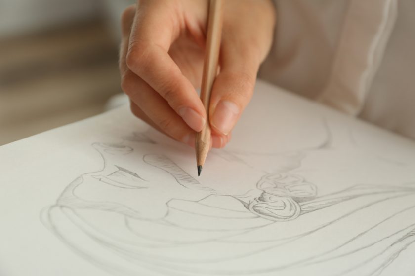 Woman drawing girl's portrait with pencil on sheet of paper, closeup