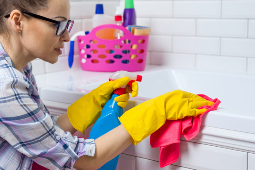 minimalist mom cleaning bathroom tub with gloves and microfiber cloth