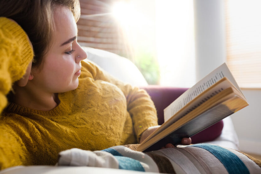 Woman reading a book lying on the couch in the living room