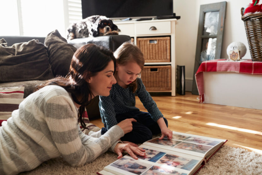 mom and young daughter laying on the floor, looking at photo albums on new year's eve