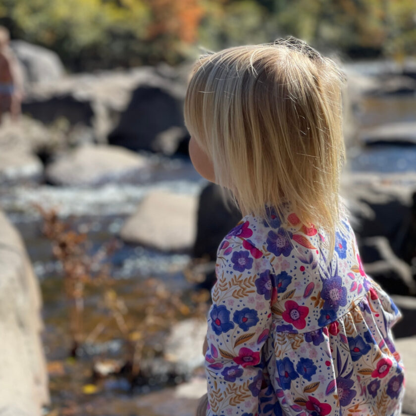 unschooled 3-year-old on a family outing to a local river, sitting on a rock looking at the water