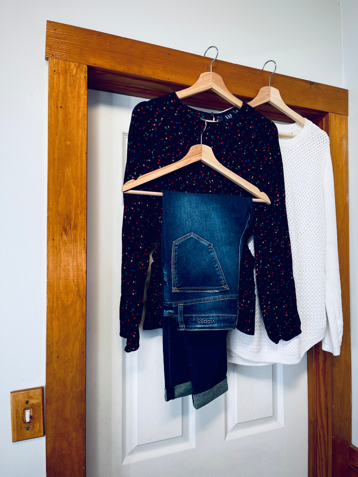 white sweater, black sparkle dress top, jeans, hanging on hangers over a door frame