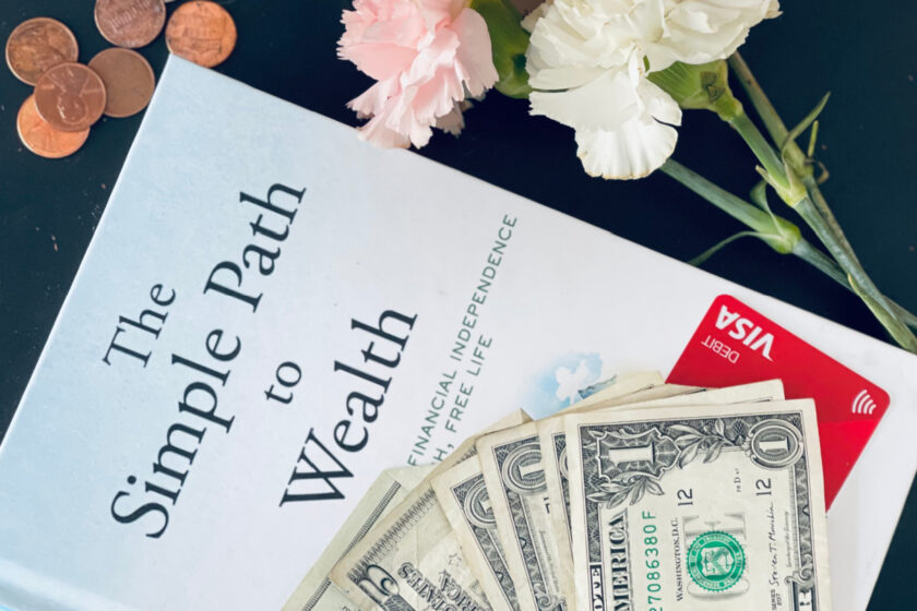 JL Collins' The Simple Path to Wealth, with dollar bills, a Visa card, pennies and carnations