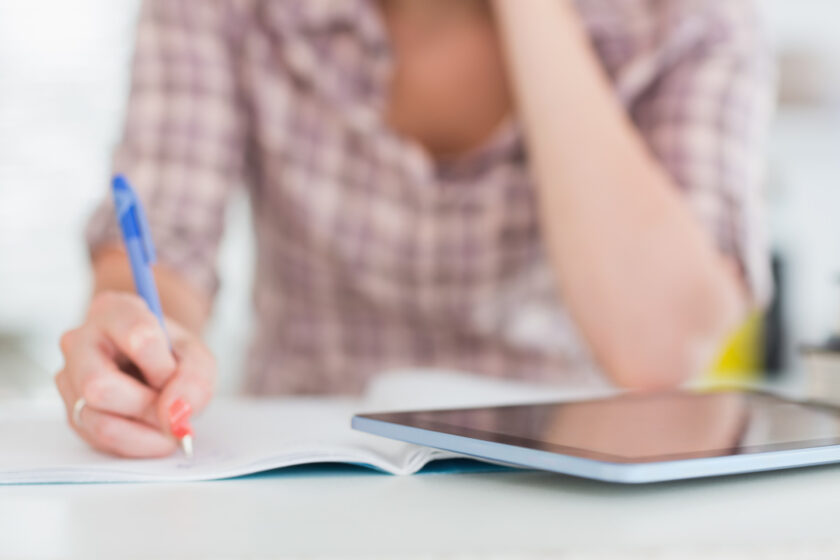 woman creating her minimalist morning routine, writing it down in a notebook with a tablet nearby