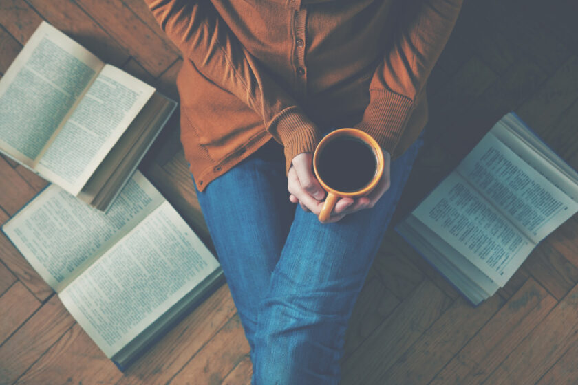 woman sitting on the floor, drinking coffee and reading as part of her simple morning routine