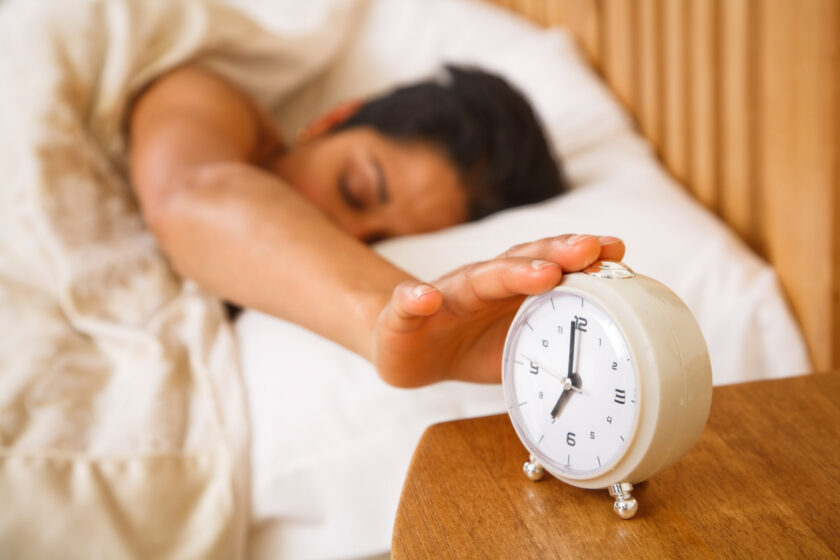 woman turning off alarm clock, trying to get up early for a morning routine