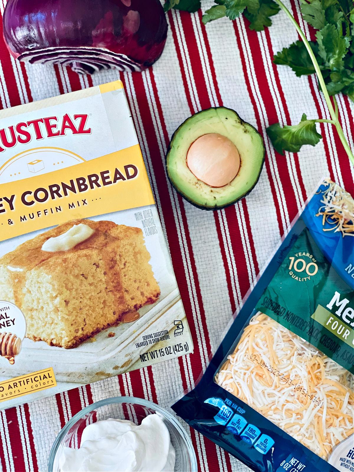 various chili toppings laid out on dish towel: cornbread, mexican cheese, avocado, cilantro, red onion, sour cream