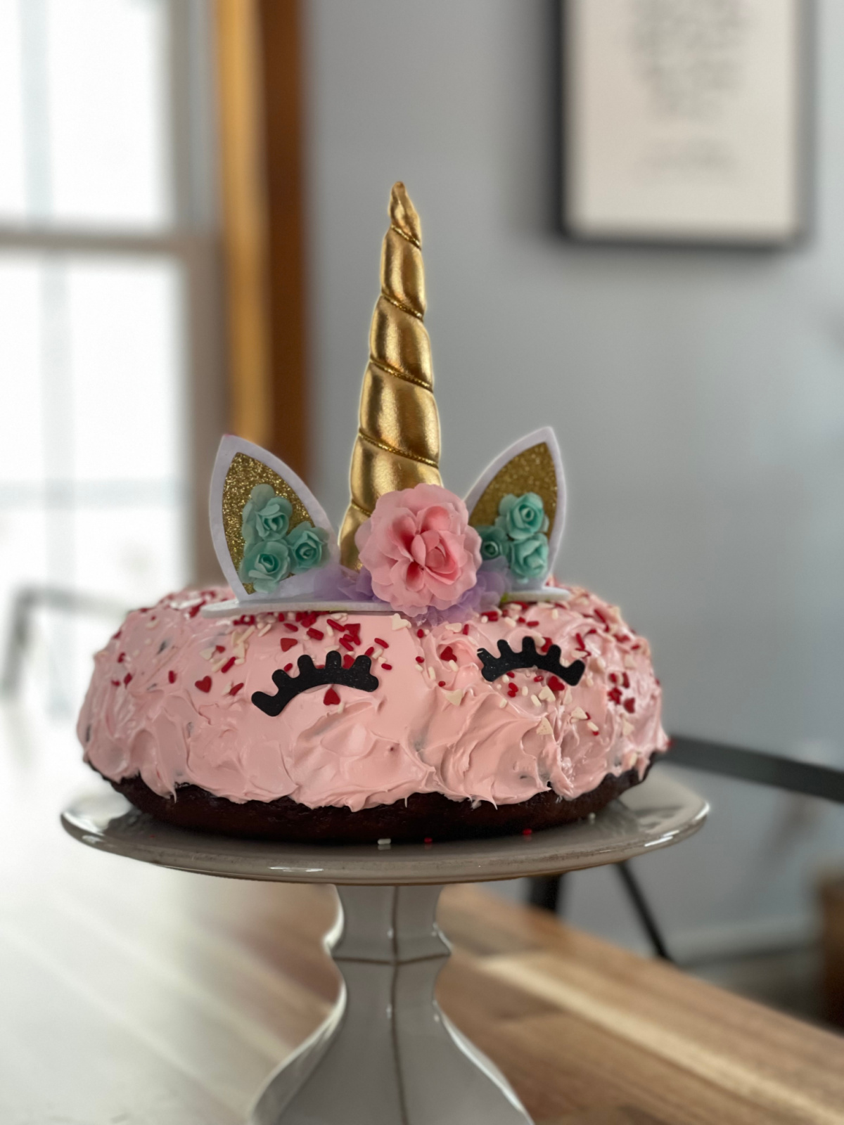 pink unicorn birthday cake on gray cake stand on table