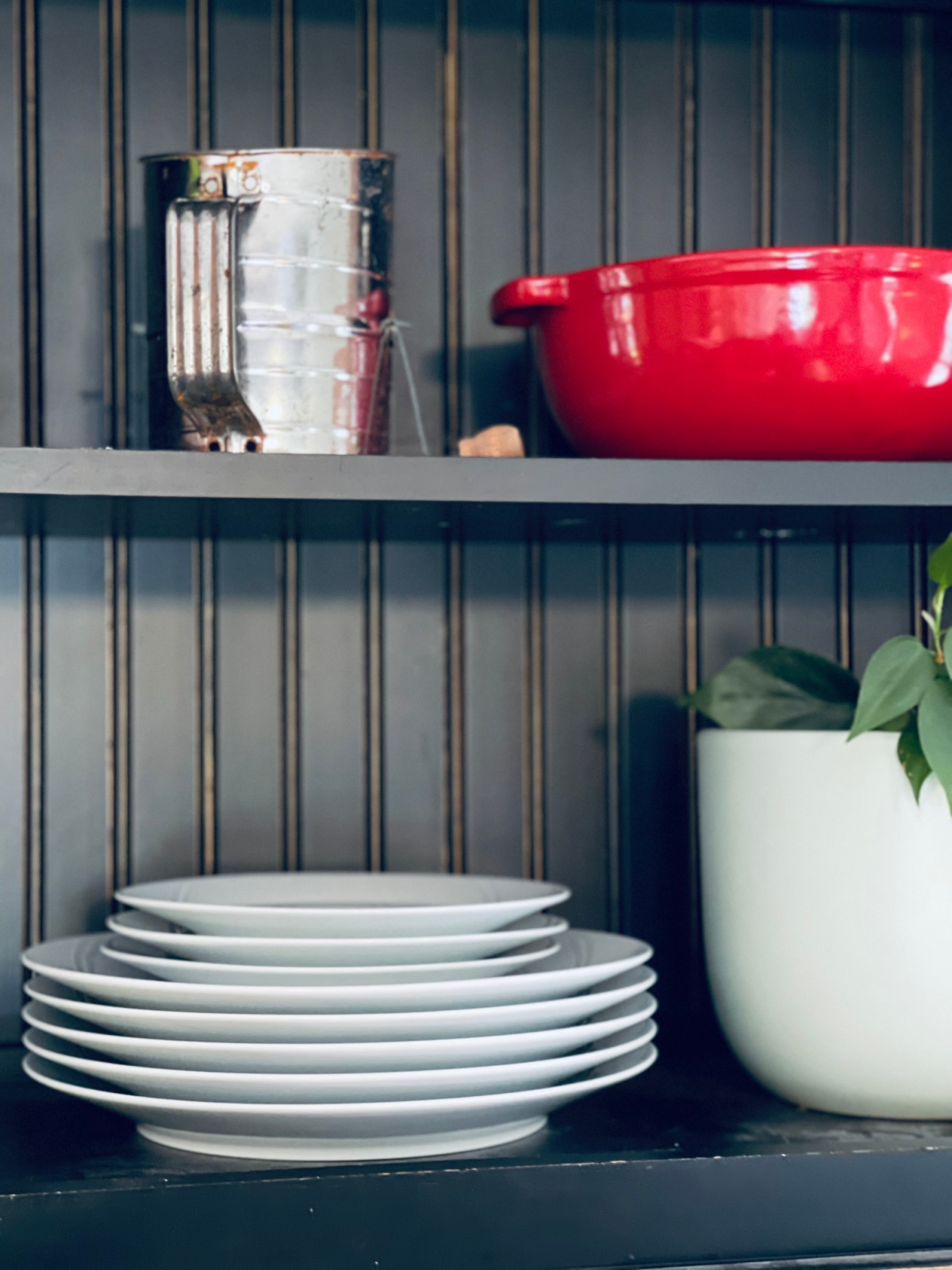 dinner plates stacked on shelf with plant, sifter and red decorate bowl