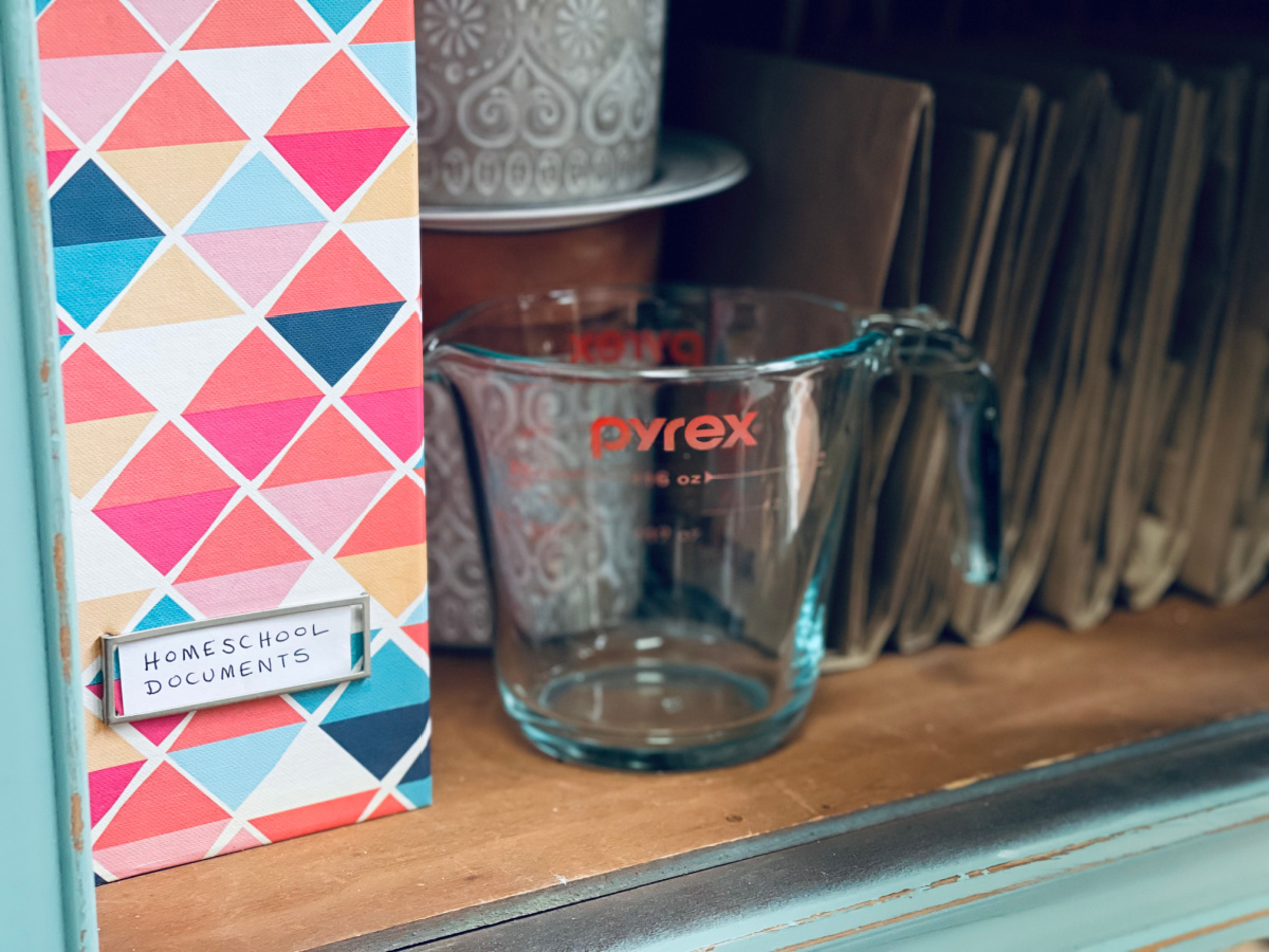 "homeschool documents" label on magazine holder in cabinet next to pyrex and brown paper bags