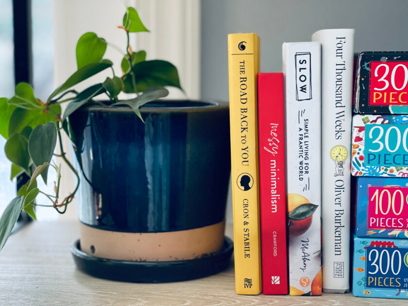 books on ways to make life easier, from slow living to minimalism to personality types, sitting next to plant on shelf