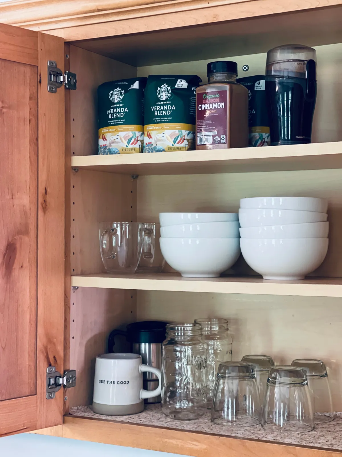 open minimalist kitchen cabinets with coffee, cinnamon, white bowls and clear glasses